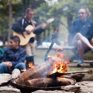 campfire in the foreground with campers hanging out in the background